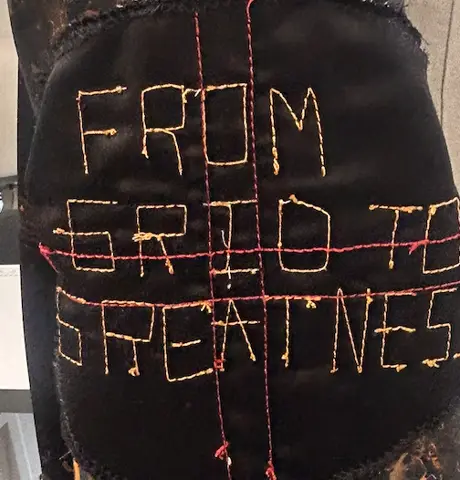 Embroidered words From Grid to Greatness on black fabric