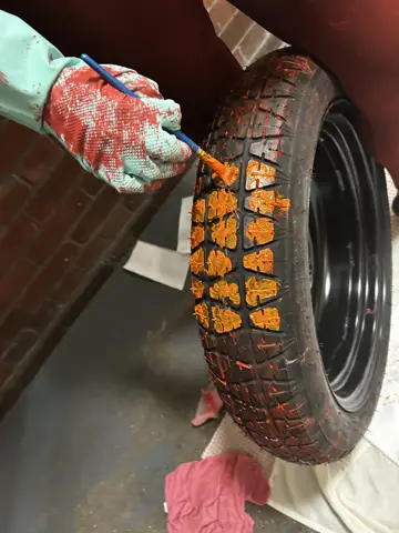 Hands painting a tyre with orange fabric paint